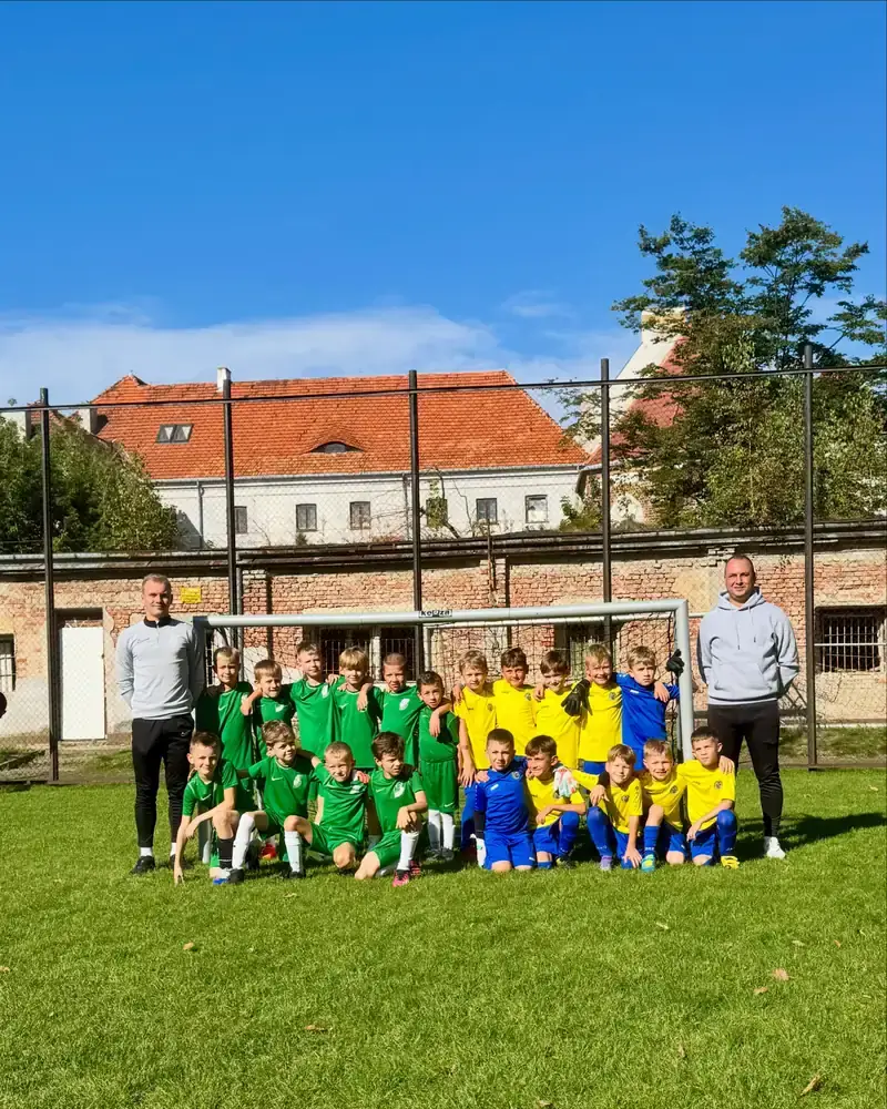 Dwie grupy młodych piłkarzy oraz ich trenerzy pozują do zdjęcia na boisku.
