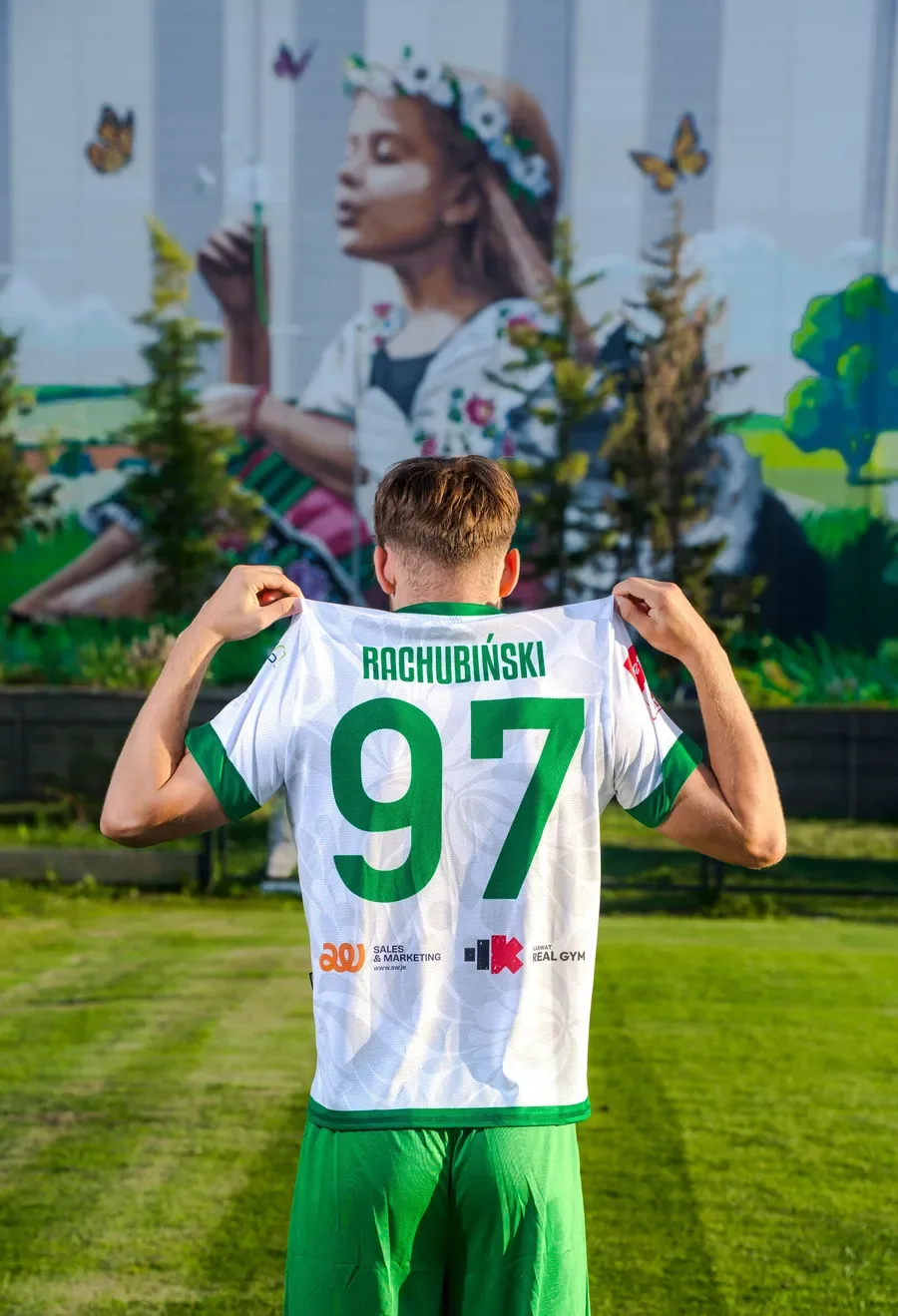 Koszulka meczowa z logotypami sponsorów Zawodnik Pelikana Łowicz prezentuje tył białej koszulki meczowej z nazwiskiem i numerem 97 oraz logotypami sponsorów klubu.
