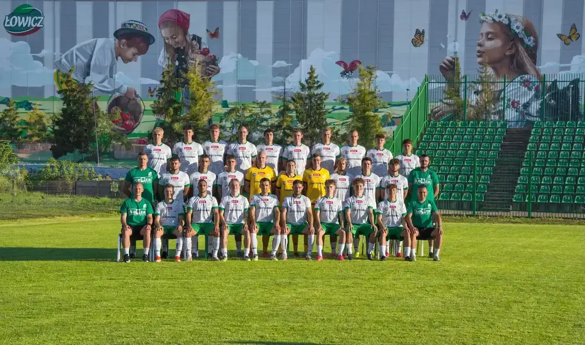 Pelikan Łowicz — pierwsza drużyna Drużyna seniorów Pelikana Łowicz pozująca do wspólnego zdjęcia na stadionie przy muralu łowickim — partnerzy biznesowi wspierają cały zespół.