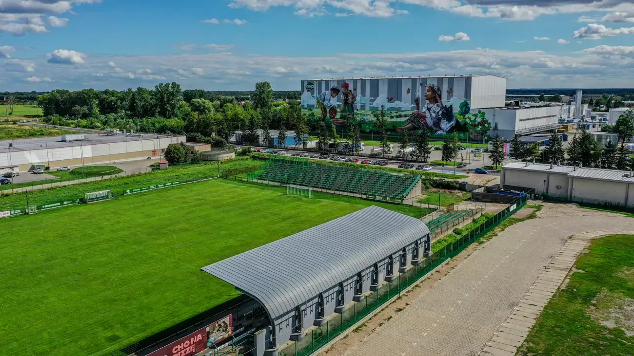 Panorama Stadionu Miejskiego w Łowiczu z drona — zadaszona trybuna główna i boisko z naturalną trawą.