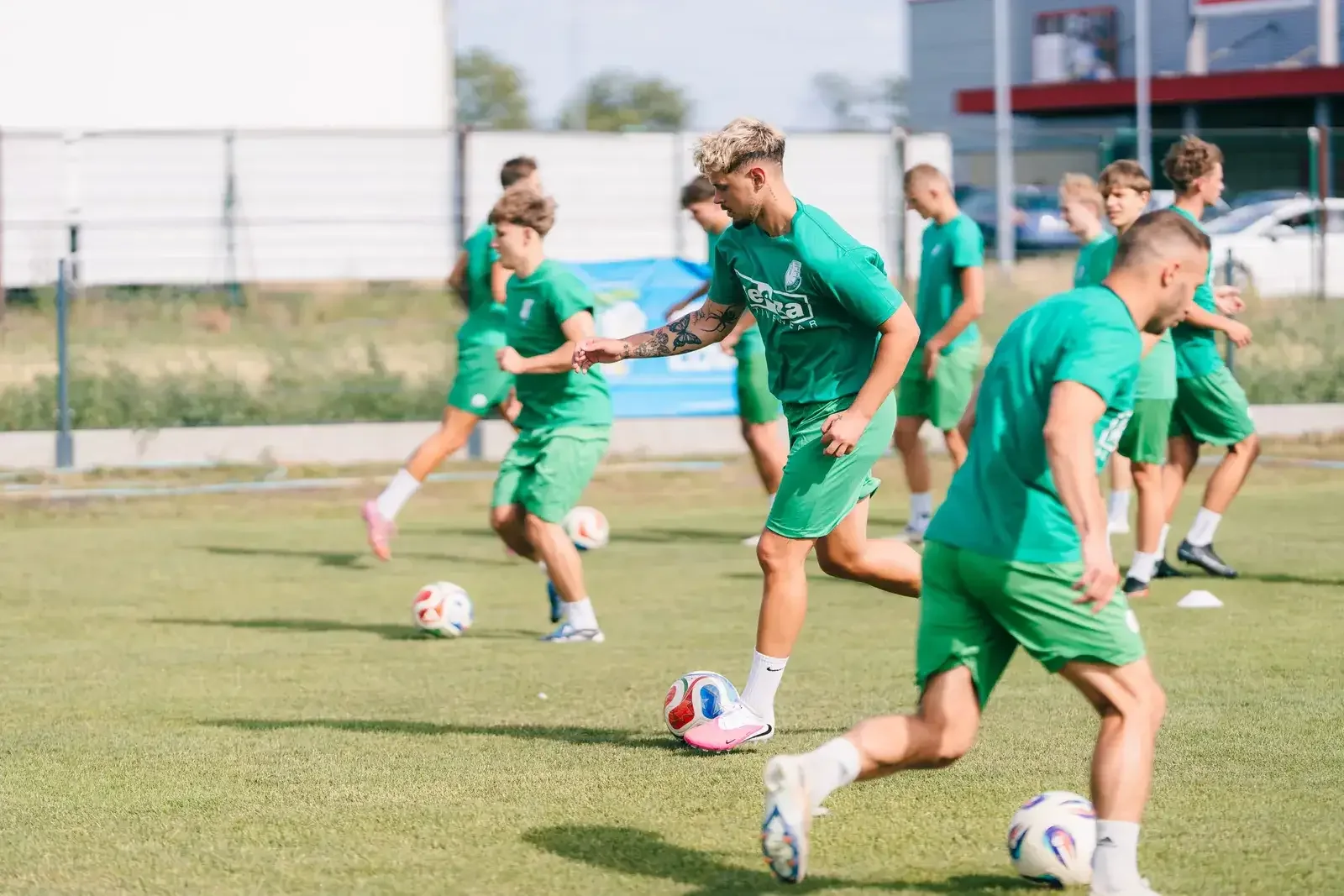 Trening Pelikana Piłkarze Pelikana Łowicz w zielonych strojach trenują z piłką na boisku.