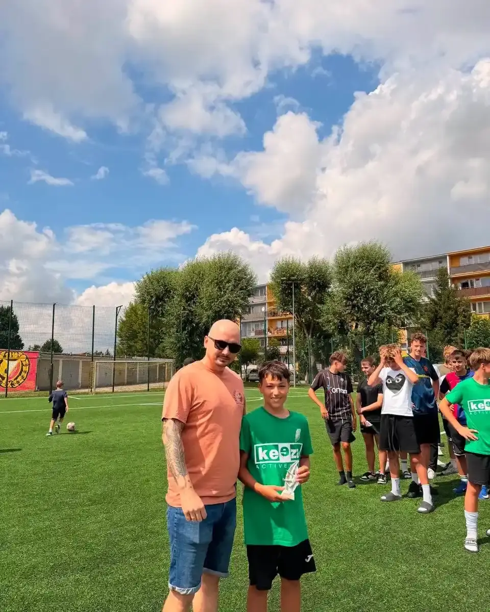 Młody zawodnik i dorosły mężczyzna trzymają trofeum na boisku podczas turnieju Zatorze Cup.